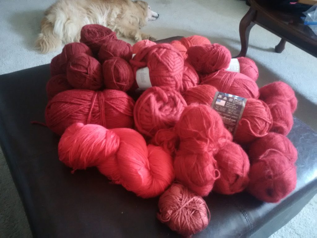 My red yarn stash that nearly overflows my ottoman, with Ollie laying in the background.