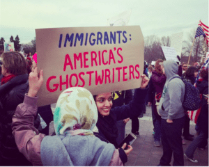 Two female protestors after the executive order was announced on the streets holding a sign that says Immigrants: America's Ghostwriters. Taken from Publishers Weekly