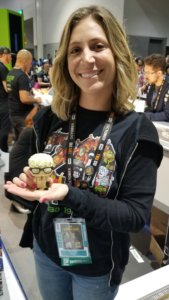 Megan Harris at the ThinkGeek booth at SDCC 2019 holding a Funko of Post-it Note Man from the movie Office Space