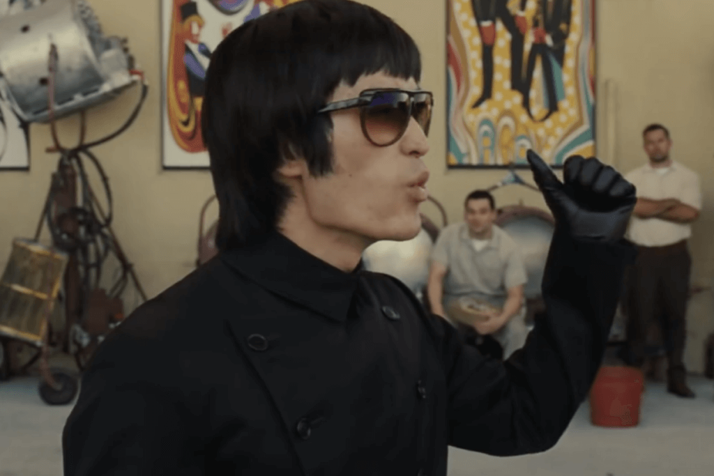 Mike Moh as Bruce Lee points with his thumb wearing his black Kato costume.