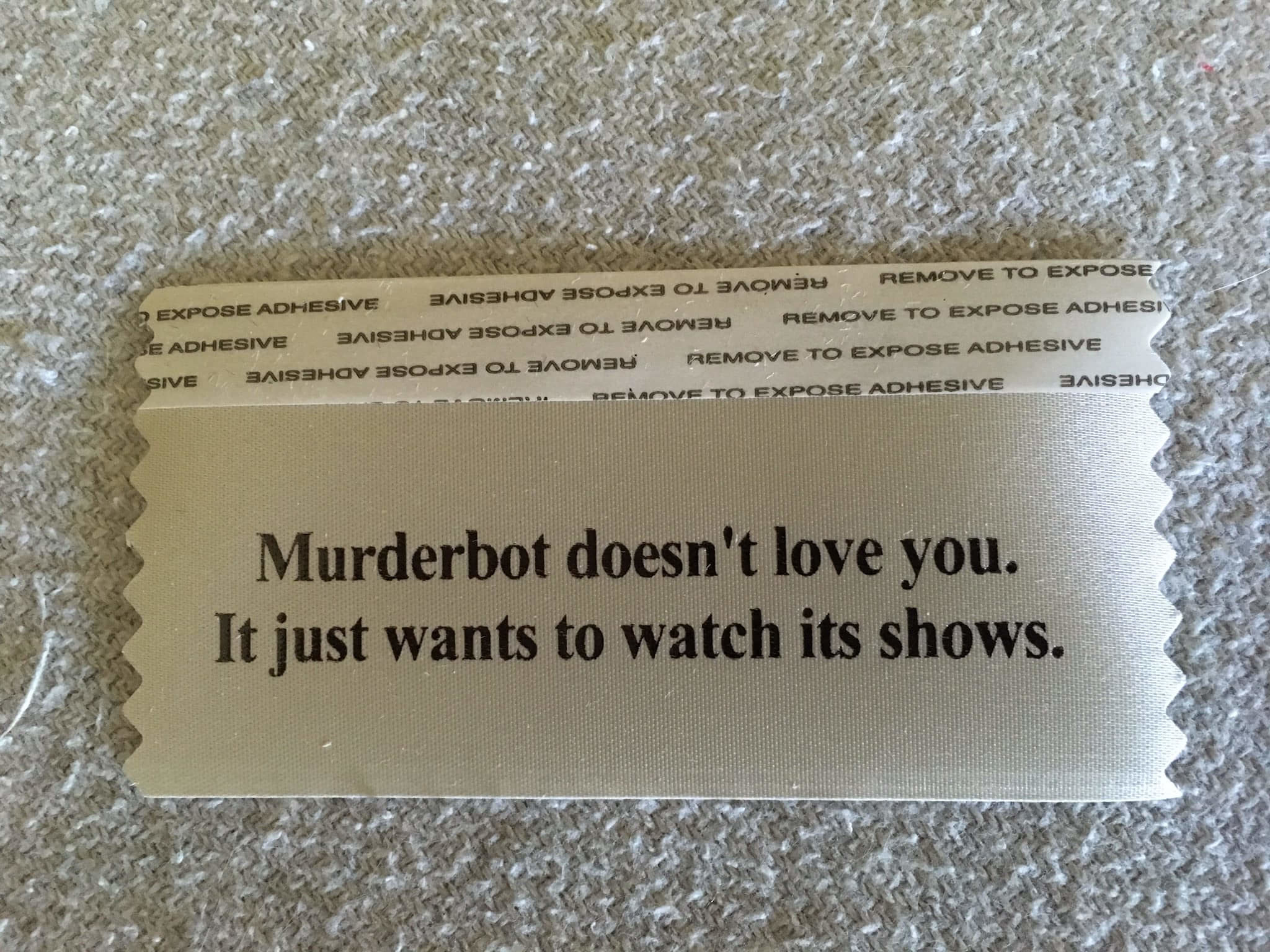 a badge ribbon that reads "Murderbot Doesn't Love you. Murderbot just wants to watch its shows.