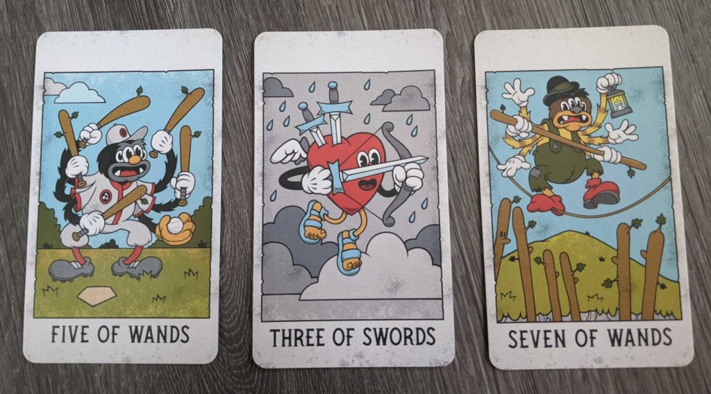 Three cards from the Mystical Medleys deck: the 5 of wands, the 3 of swords, and the 7 of wands