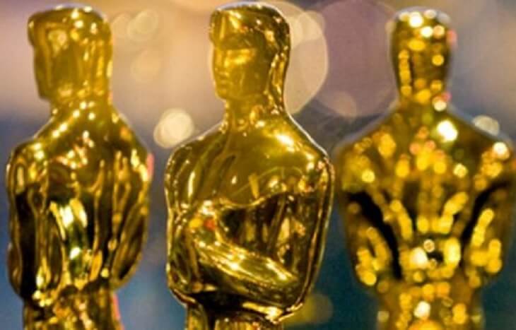 Three gold Oscar statuettes with lens flare.