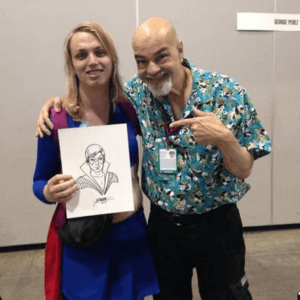 A blonde woman in a Supergirl costume holding a sketch of Nightwing, while being hugged by George Pérez, a bald man with a grey beard and a hawaiian shirt.