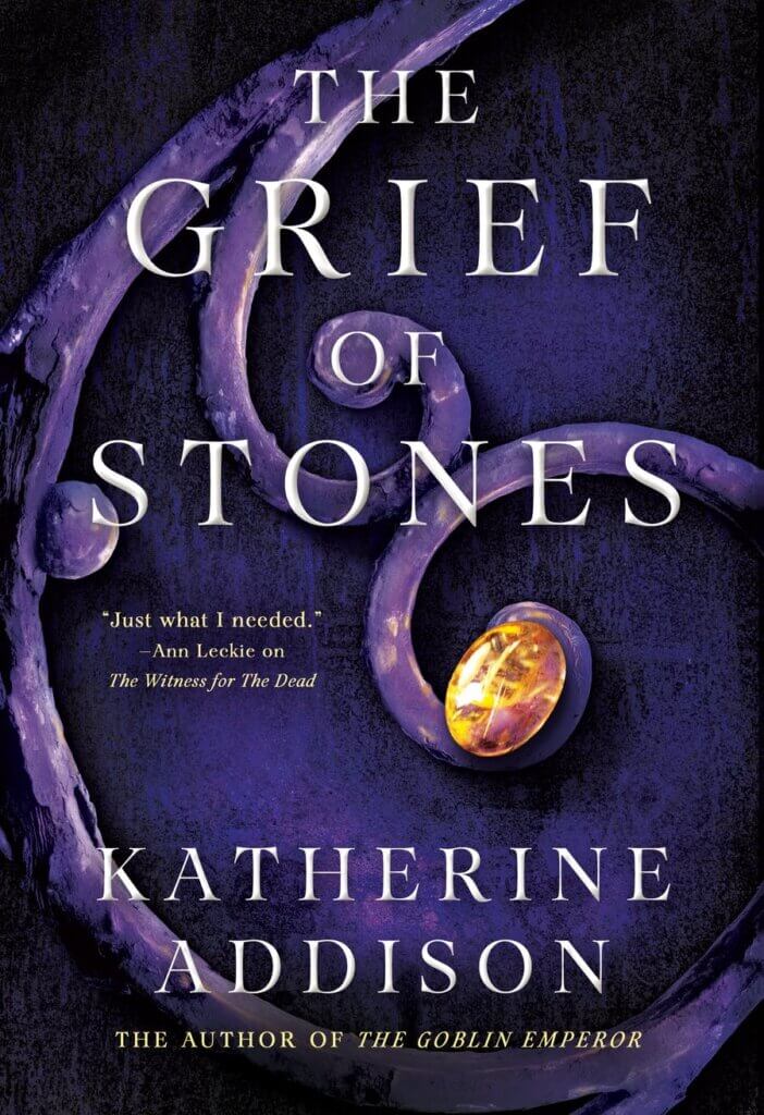 swirling stone or metalwork with one glowing amber oval provides the backdrop to the title and author on the cover of the Grief of Stones by Katherine Addison. 