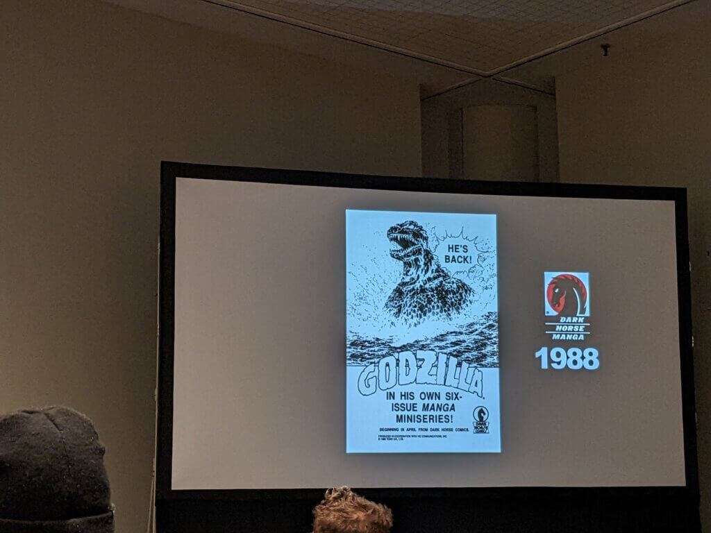 Photo of screen showing powerpoint slide with Dark Horse logo and the flipped Godzilla manga from 1988.