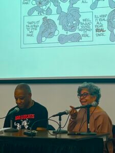 Emily Lauer's photo shows Calvin Reid interviewing Barbara Brandon Croft at MoCCA Fest 2023 under a screen showing images from Brandon-Croft's comic, Where I'm Coming From. 