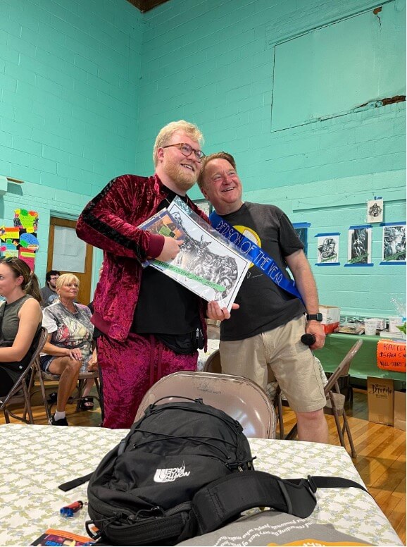 Two smiling white men posing together with bat-shaped art, one younger and one older.