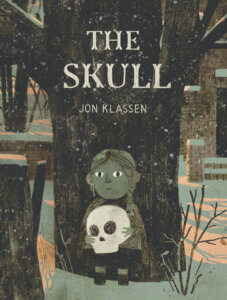 The cover of The Skull by Jon Klasses shows a solemn looking child with braids holding a skull in front of a dark tree