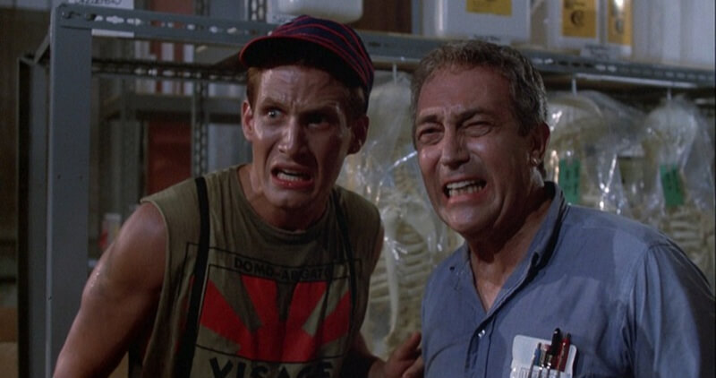 Still from the film The Return of the Living Dead showing two frightened men in a warehouse.