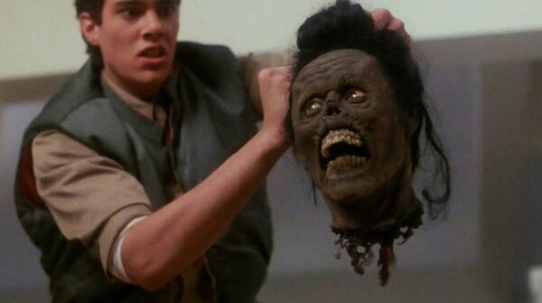 Still from the film Return of the Living Dead Part II. A man holds a severed zombie head.