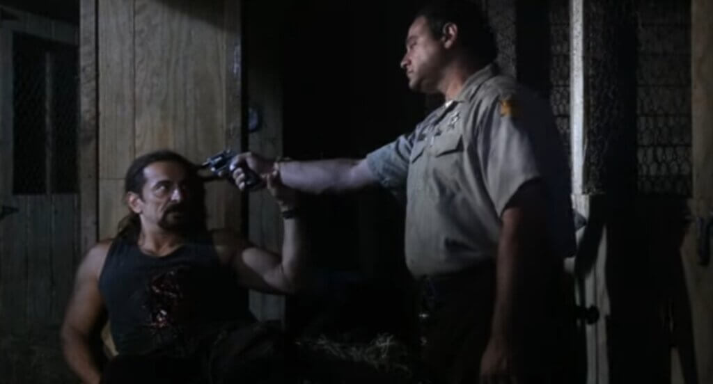 Still from the film Children of the Living Dead. Shows Tom Savini's character pressing another man's gun to his head.