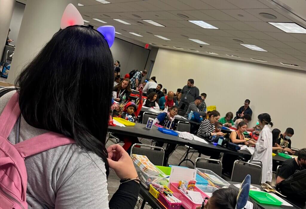 Children and adult con-goers construct wooden Devil Dinosaurs at NYCC 2023. 
