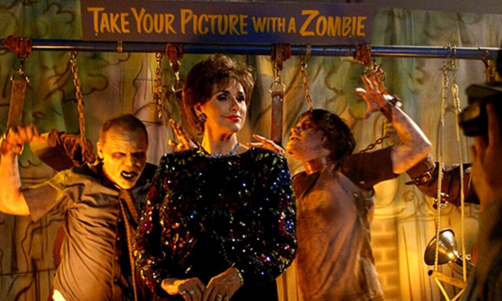 Still from the film Land of the Dead. A woman poses for a "Take Your Picture With a Zombie" attraction (zombies played by Simon Pegg and Edgar Wright in cameo)