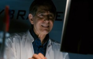 Still from the film Return of the Living Dead: Necropolis. Shows a man in a lab coat at a computer.