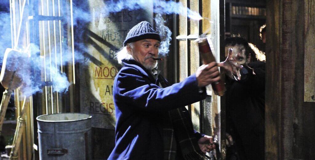 Still from the film Survival of the Dead. A man thrusts a stick of dynamite into the grasping hand of a zombie.