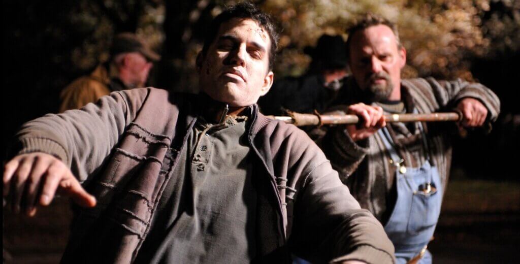 Still from the film Survival of the Dead. A man attacks a zombie with a farming implement.