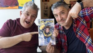 Photo of Patton Oswalt and Jordan Blum with enthused faces holding an issue of Archie is: Mr. Justice #1 between them and pointing at it.